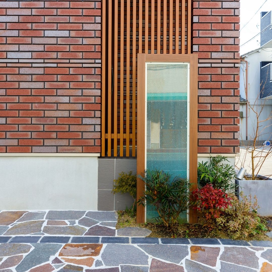玄関を目隠しする木目のスリットフェンスと、会社の表札を入れたガラスパネル。