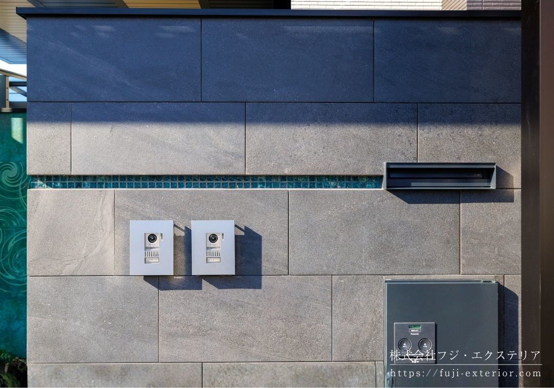 門柱は外周と同じタイルを貼り連動性を。ポスト、インターホンを各２台取付け、表札部分にはグリーンのモザイクタイルでアクセントを。