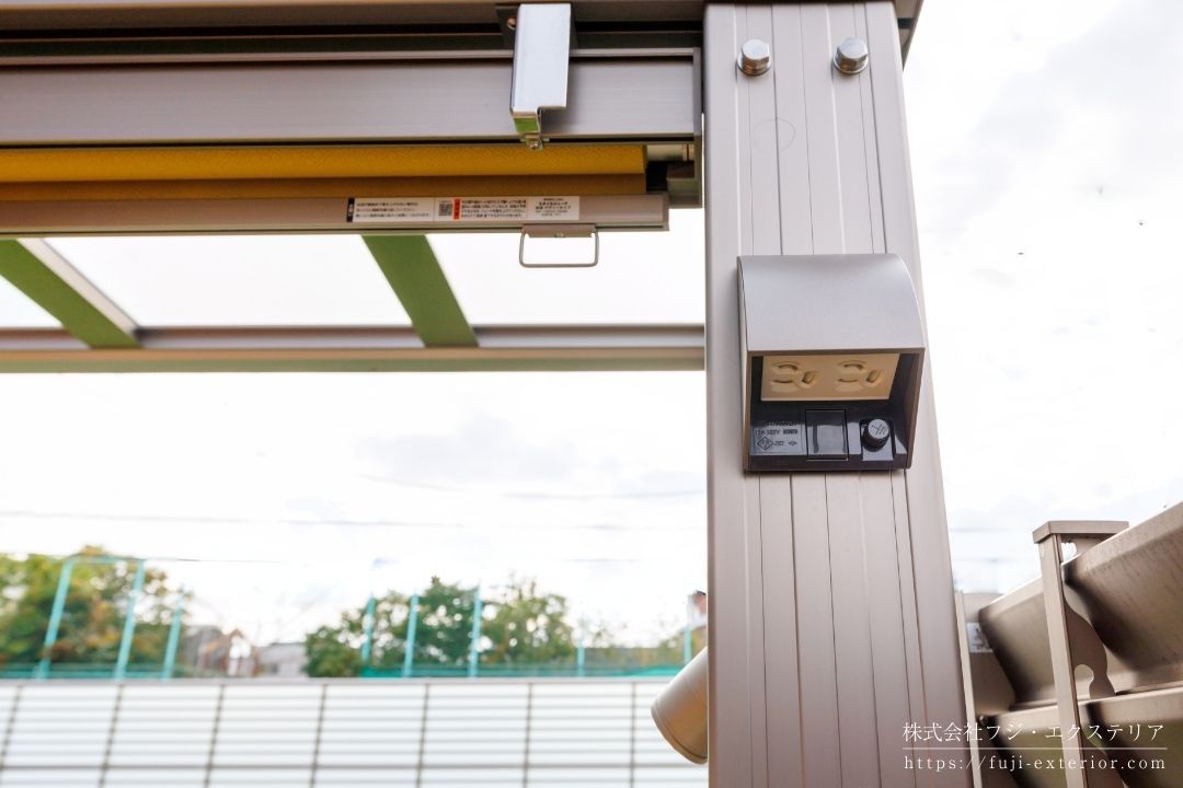 L字型樹脂デッキを覆う3台用カーポートの設置事例。夜間照明用のスポットライト、100V防水コンセント、対角の柱から操作可能な防水スイッチを備えた、多機能なアウトドアリビングの電気設備施工。