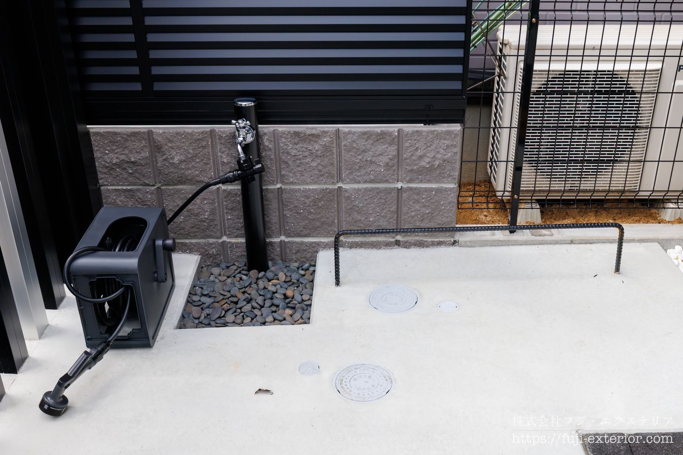 立水栓の排水パン(水受け)は落とし込みにして砂利を敷きました。チョットした事ですが、水撥ねもしにくくなります。
右側に見える黒いパーツは、鉄筋を曲げてコンクリートに埋め込んだ盗難防止用フックです。錆止め処理を施し、黒色塗装で仕上げています。自転車の盗難防止で、チェーンでタイヤとフックを固定できます。
市販品もありますが、こちらは鉄筋加工と塗装のみで製作しているため、コストを抑えつつ実用性の高い対策になっています。