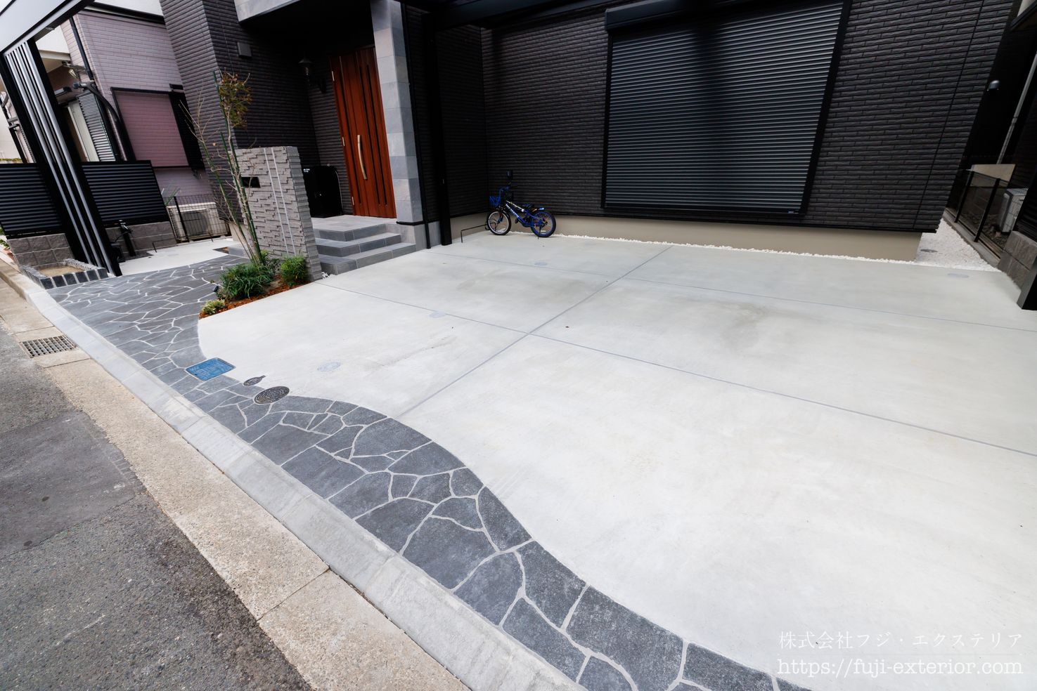 アプローチとガレージには、ブラック系の乱形石をウェーブ形状で施工。重厚感のある素材に柔らかな動きを与え、上質で表情豊かな空間に仕上げています。一石一石をハンマーで割り、微調整しながら納める手仕事は、熟練の職人技があってこそ実現する床仕上げです。