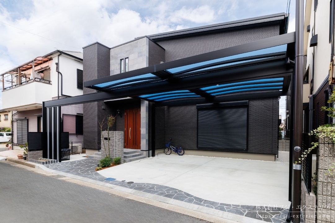 ファサード空間全体を整える全長12mフレームのカーポート屋根は三協アルミ U.スタイルアゼスト・梁延長納まり。ブラック&シルバーのモノトーン配色で住宅ともシックに調和しています。